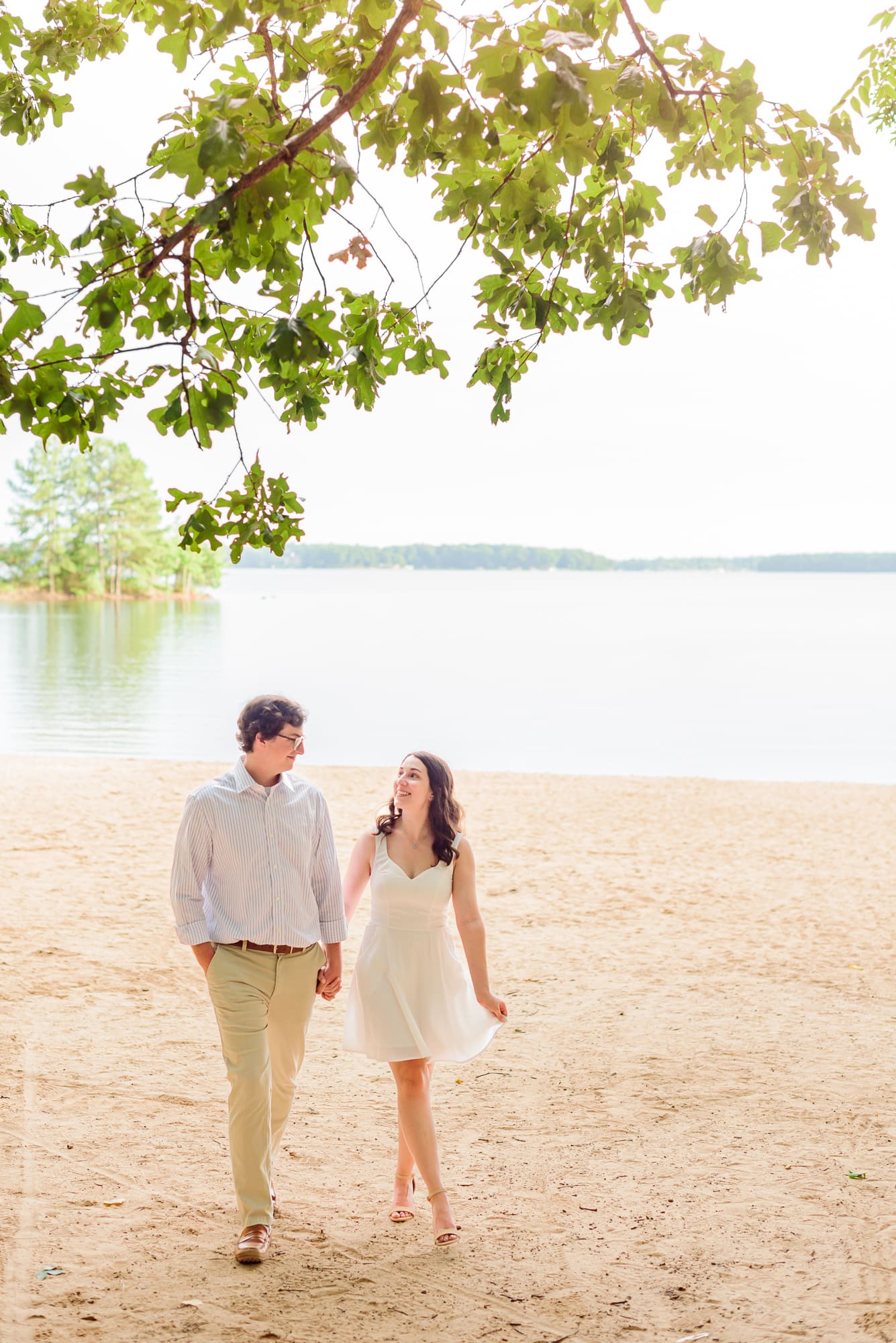 The bride and groom walk hand in hand on the beach during their Jetton Park engagement photos.